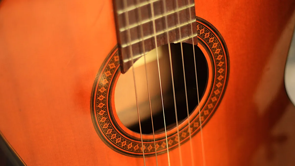 boca e roseta de um violão de tampo alaranjado com as cordas de nylon à vista