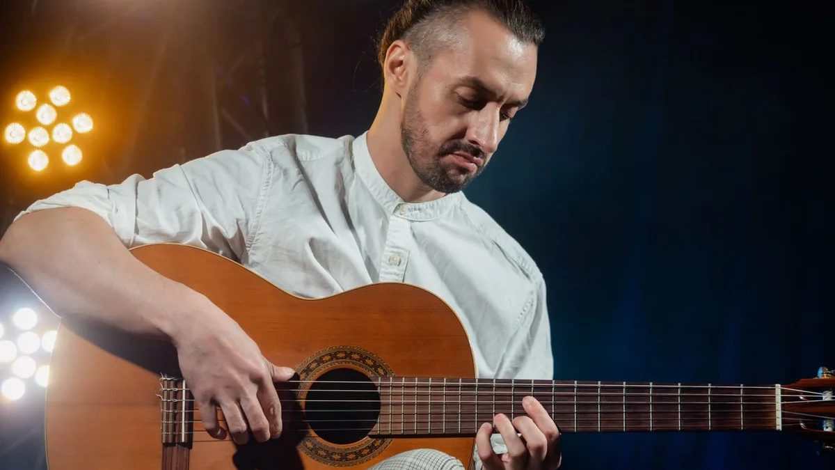 violonista de camisa branca tocando um violão acústico sob luzes de palco