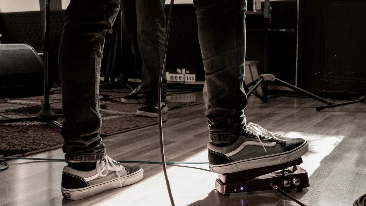pé de guitarrista com tênis preto pisando em um pedal de balanço no chão de madeira de um estúdio