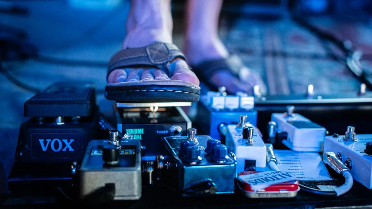 pé de guitarrista pisando em um pedal de efeito ao lado de um pedal wah Vox em uma pedalboard